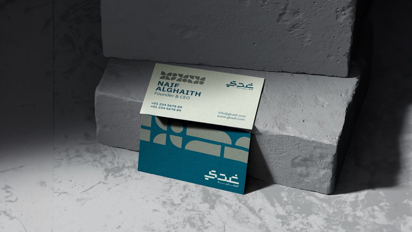 Ghadi business card in teal and cream, propped against concrete blocks.